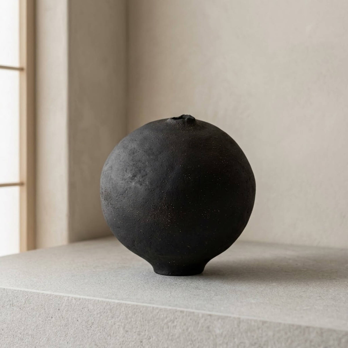 Hand-built black spherical stoneware vase with matte tactile finish in a minimalist interior setting by Authentico Ceramics