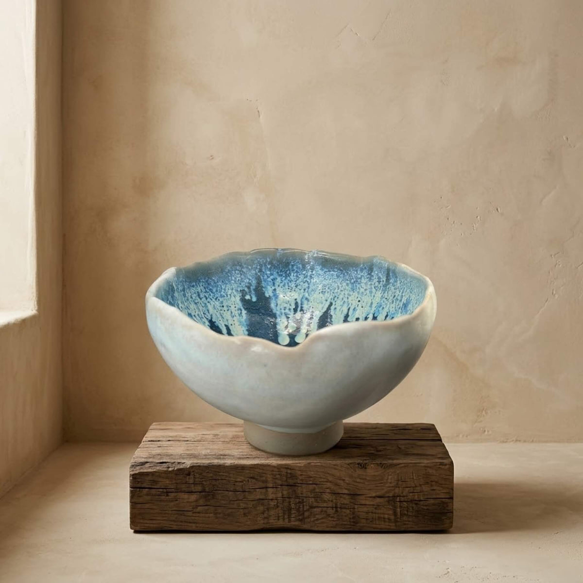 Hand-sculpted stoneware footed bowl with undulating wavy rim and deep turquoise crystalline mineral glaze interior placed on a rustic wood pedestal in a Wabi-Sabi interior by Authentico Ceramics