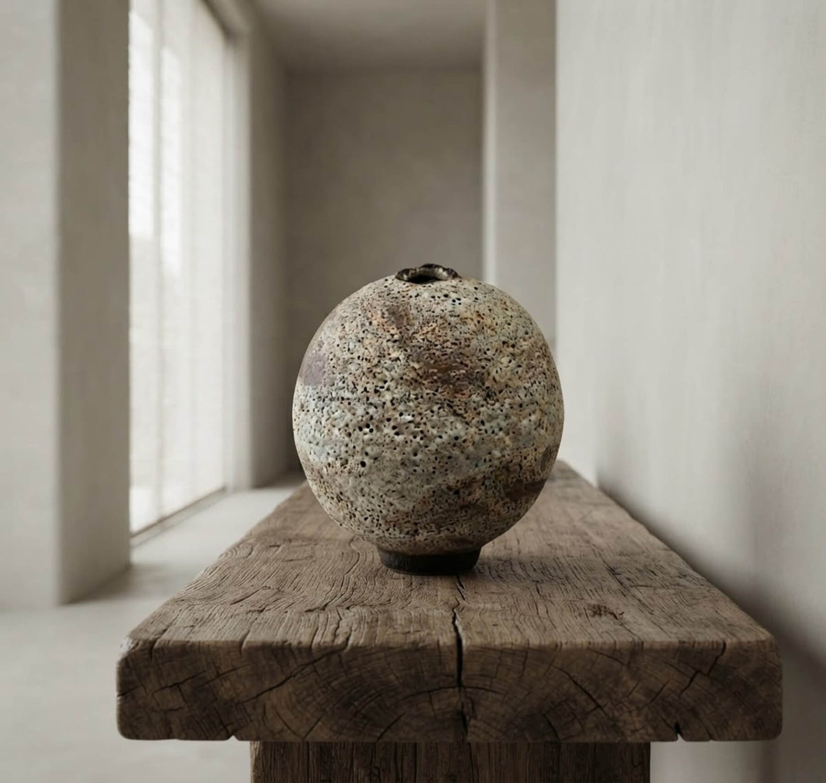 Spherical porous ceramic art sculpture in earthy tones, placed in a serene minimalist Japandi architectural gallery space.